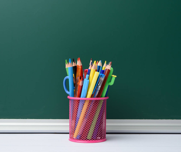 рожеве канцелярське скло з різнокольоровими дерев'яними олівцями та ручками, фон з крейдової дошки, місце для тексту
 - Фото, зображення