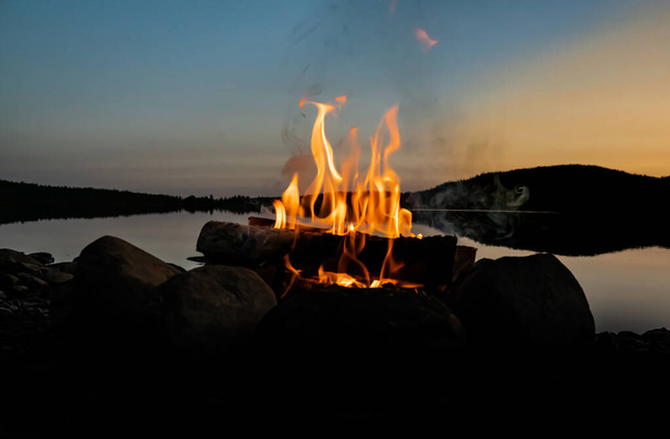 Gezellig kampvuur op het strand van een meer in de avond. . Hoge kwaliteit foto - Foto, afbeelding