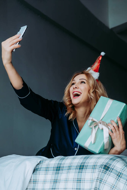 woman with christmas gifts. celebrating christmas through the phone. Skype chatting during Christmas. The girl received a gift through delivery. Girl wishes merry christmas to relatives via phone - Φωτογραφία, εικόνα