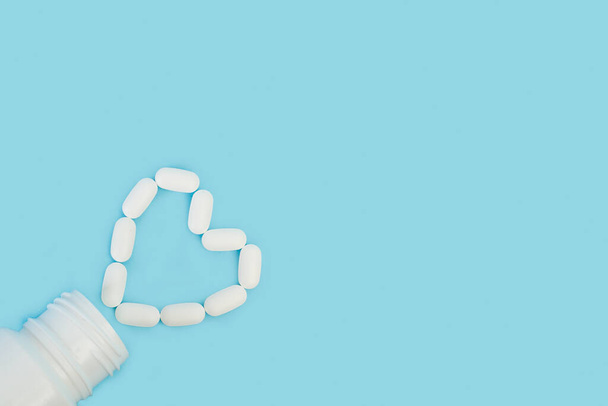 Orvosi tabletták alakja szív egy műanyag palack egy világoskék háttér - Fotó, kép