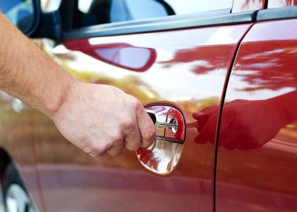 Male hand inserting a key into the door lock of a red car closeup - Foto, Imagen