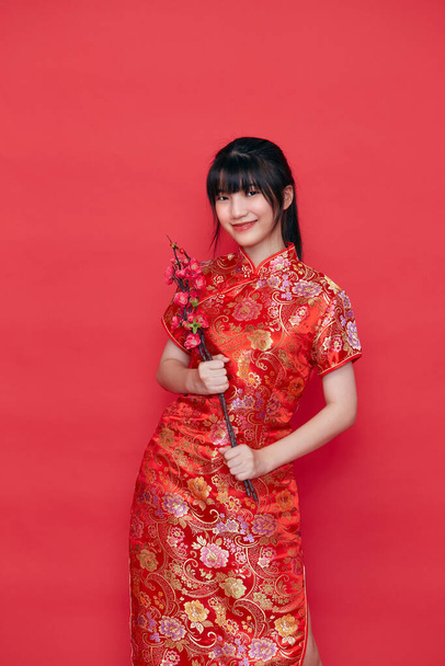 Krásné asijské ženy v červené tradiční čínské šaty s držení sakura větev na červeném pozadí, čínský nový rok 2021 - Fotografie, Obrázek