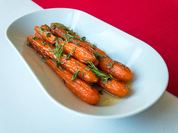 Lasitetut porkkanat tilliä ja timjamia valkoisella pöytäliinalla ja punaisella pöytäliinalla - Valokuva, kuva