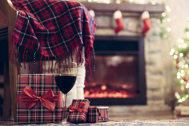 Woman legs in a socks covered plaid sitting and relaxation on armchair near fareplace and christmas tree with glass of wine after finishing pakking gift boxes for family. Bottom view. - Фото, зображення