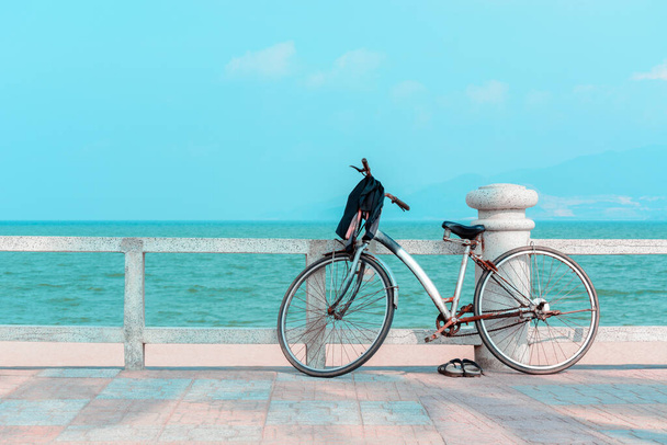 Rusty bike with slippers on pier overlooking the blue sea. - Фото, изображение