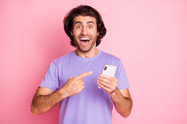 Photo of handsome funny model directing fingers smartphone proposition wear violet isolated on pink color background - Foto, imagen