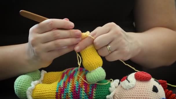Naaien van een gehaakte pop. Close-up op de hand van een vrouw met behulp van een breinaald om een gehaakte pop met een wollen garen naaien. - Video