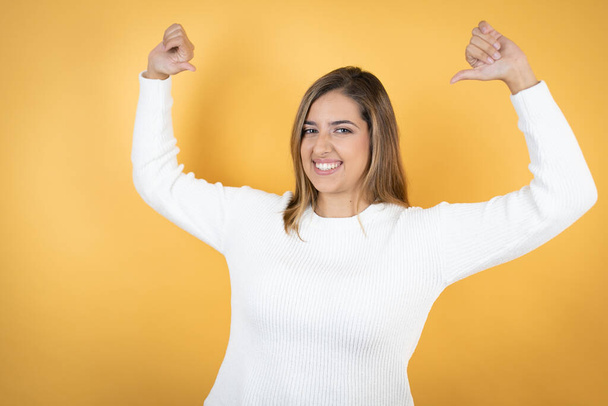 Young caucasian woman over isolated yellow background looking confident with smile on face, pointing oneself with fingers proud and happy. - Fotografie, Obrázek