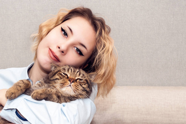 Happy blond girl portrait with a cat on the sofa - 写真・画像