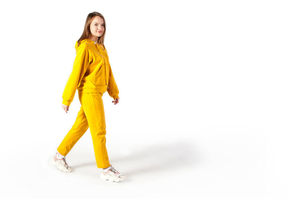 Chica adolescente caminando en ropa deportiva amarilla sobre fondo blanco - Foto, Imagen
