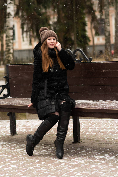 Happy young woman sitting on bench in winter outdoors - Fotó, kép