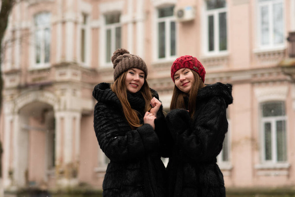 Two young girls posing together. Fashion portrait of two sisters hugs and having fun winter time, wearing fur coat. best friends couple outdoors, snowy weather - Foto, imagen