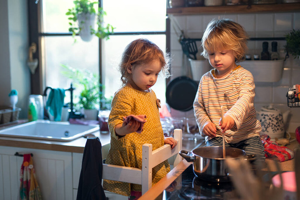 Small boy and girl indoors in kitchen at home, helping with cooking. - Фото, изображение
