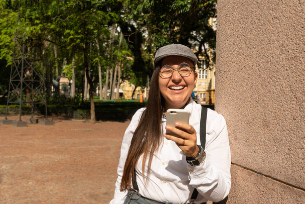 Чабби уникальная женщина с подтяжками смеется и держит мобильный телефон. На улице в солнечный день. Технологии, социальные сети, концепция подключения. - Фото, изображение