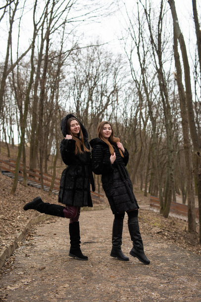 Two young girls posing together. Fashion portrait of two sisters having fun in winter time, wearing fur coat. best friends couple outdoors, snowy weather - Фото, зображення