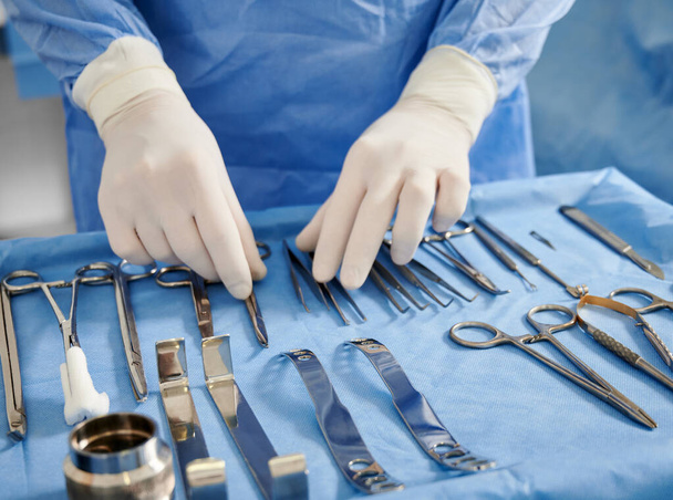 Close up of plastic surgeon in sterile gloves getting ready medical instruments for operation. Doctor preparing scissors, forceps and scalpels for surgery. Concept of plastic surgery preparation. - Valokuva, kuva