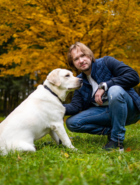 Man with white retriver poses to camera in park. Best friends forever concept. Closeup. - Foto, afbeelding