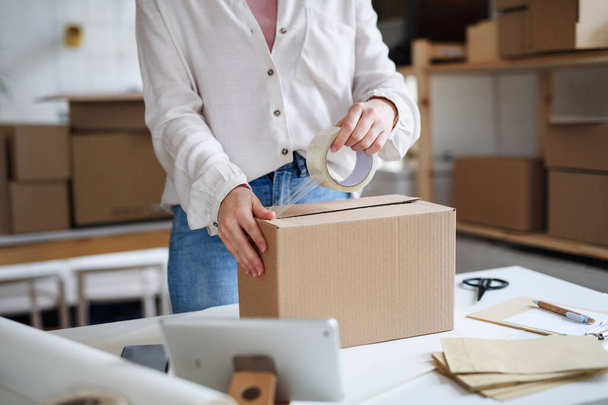 Unrecognizable woman dropshipper working at home, packing parcels. Coronavirus concept. - 写真・画像