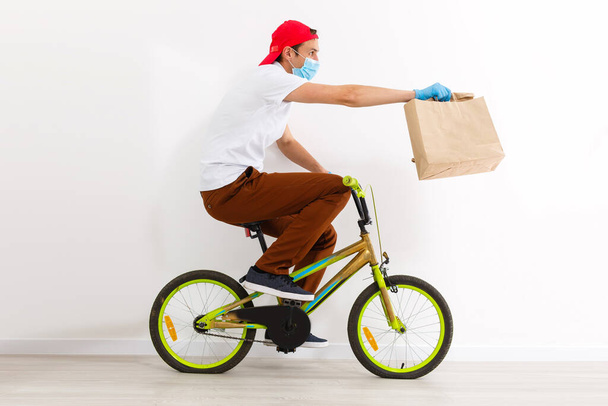 保護マスクの男が自転車で食べ物を配達している。オンラインショッピングとエクスプレス配達。隔離 - 写真・画像
