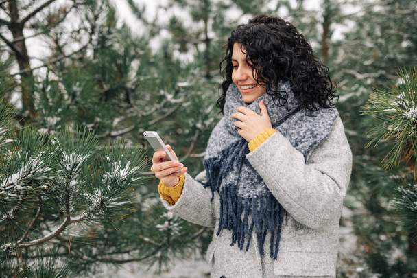 Mladá žena používá svůj mobil v zasněženém zimním parku. Detailní záběr ženských zpráv a textování na jejím mobilu venku během studené zimní sezóny. Koncept lidových hraček - Fotografie, Obrázek