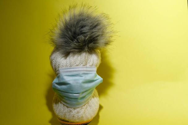 γυναικείο πλεκτό θερμό χειμερινό καπέλο με pom pom με λευκή ιατρική μάσκα, έννοια του coronavirus  - Φωτογραφία, εικόνα