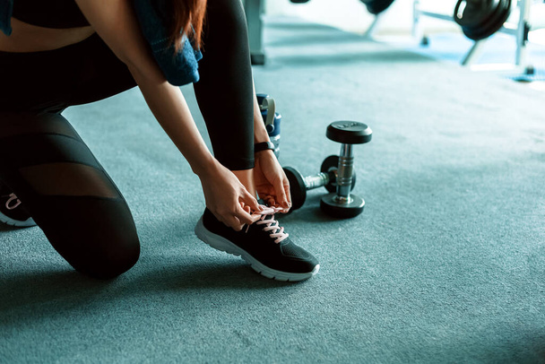woman's hands tying shoelaces on sport sneakers in gym. dumbbell and water bottle on the ground around the sport girl. - Foto, immagini