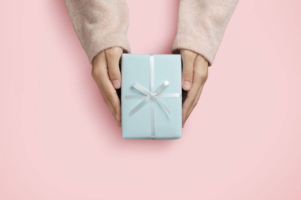 Top view of Woman hands is holding a blue gift box over pink isolated background - Фото, зображення