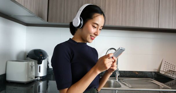 Asian women wearing headphone and listening to music in the kitchen at home - Photo, Image