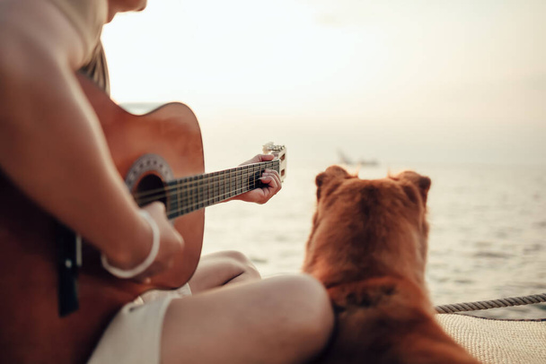 A man wear straw hat and playing guitar music song near the sea sunset with a dog pet - Zdjęcie, obraz