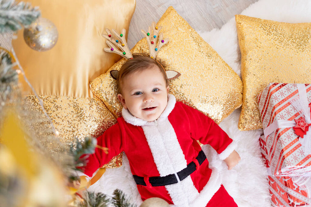 ребенок в костюме Санты лежит под елкой, концепция нового года и Рождества - Фото, изображение