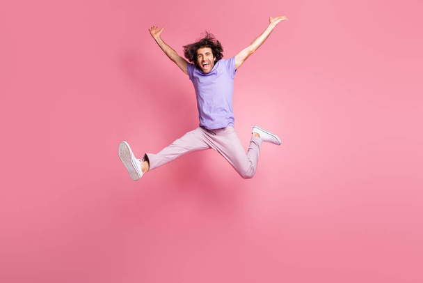 Full size photo of energetic young man raise hands jump in air success wear pink pants isolated on pink color background - Foto, Imagem