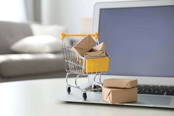 Internet shopping. Laptop and small cart with boxes on table indoors - Foto, Bild