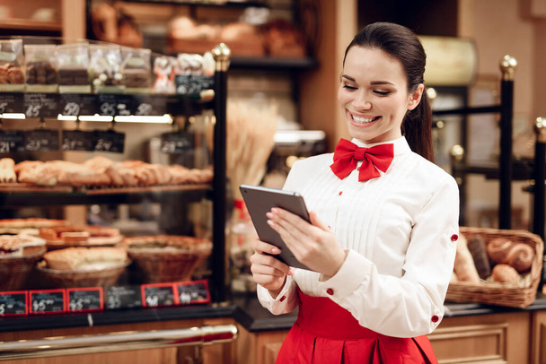 Young Smiling Woman Using Tablet in Modern Bakery. - Foto, immagini