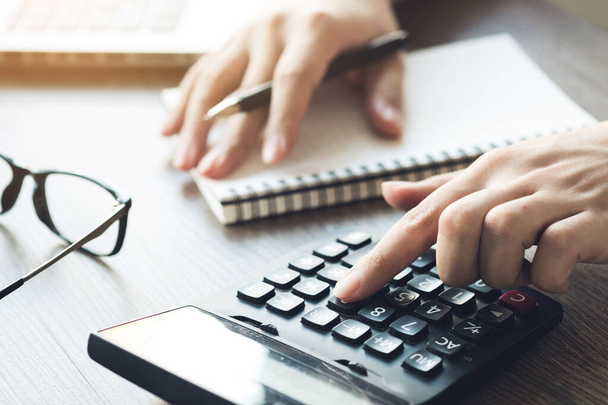 Az üzleti könyvelő a számológépet használja a bevétel kiszámításához, miközben jegyzetel a jegyzetfüzetben. A pénzügyi költség fogalmának kiszámítása. - Fotó, kép