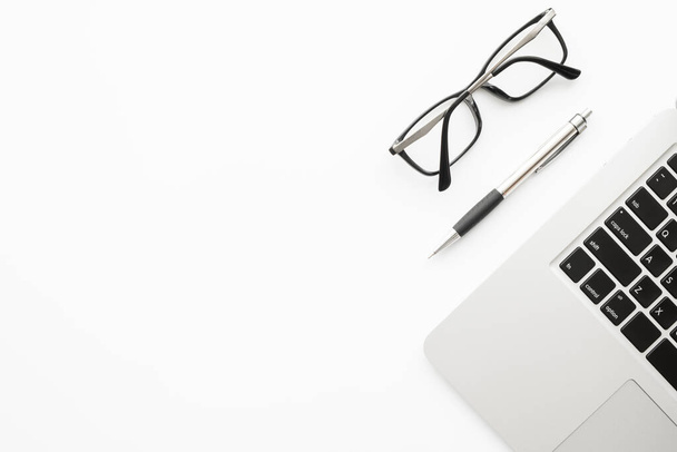 Table de bureau blanche avec ordinateur portable, stylo et lunettes. Vue du dessus avec espace de copie, plan plat. - Photo, image