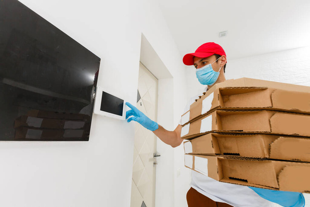 Mann vom Lieferdienst im T-Shirt, mit Schutzmaske und Handschuhen bestellt Essen und hält Pizzakartons vor weißem Hintergrund - Foto, Bild