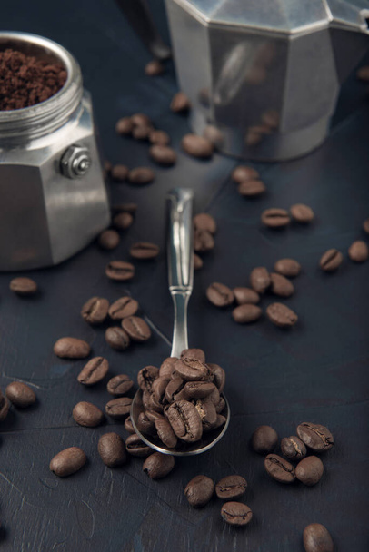 Metalen lepel met koffiebonen en koffiezetapparaat op de donkere textuur achtergrond - Foto, afbeelding