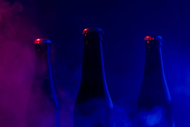 Botellas de vidrio de cerveza sobre colorido humo fondo oscuro - Foto, imagen