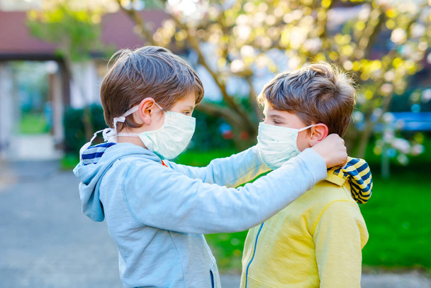 Kid boy helping brother to put medical mask on face as protection against pandemic coronavirus disease. Children, lovely siblings and best friends using protective equipment as fight against covid 19. - Φωτογραφία, εικόνα