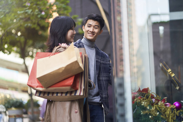 happy young asian couple walking on street in the city with shopping bags in hands - Foto, Imagem