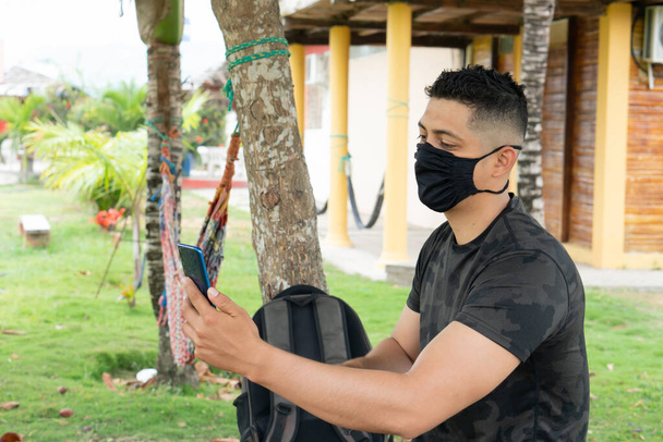 Siyah maske takan Latin bir adam, cep telefonunu açık havada kullanıyor, video görüşmeleri yapıyor.. - Fotoğraf, Görsel