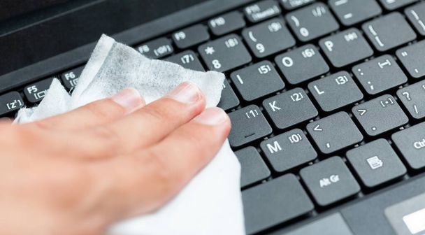 Hand disinfecting, sanitizing a modern laptop keyboard using a wet wipe. Cleaning notebook keys with a damp tissue, closeup. Office workspace hygiene practice, covid 19, corona virus safety practices - Fotó, kép