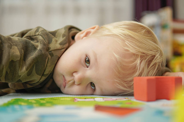 Little boy with blond hair lies sad on the floor. high quality - Фото, изображение