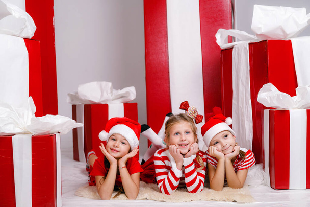 legrační holčičky kamarádky ve vánočních kostýmech na pozadí velkých červených dárečků. myšlenka a koncept šťastné dovolené, Nový rok, přátelství a dětství. - Fotografie, Obrázek