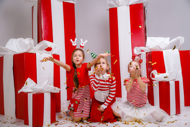 śmieszne dziewczynki lfriends w strojach świątecznych na tle dużych czerwonych prezentów. idea i koncepcja szczęśliwego urlopu, Nowego Roku, przyjaźni i dzieciństwa. - Zdjęcie, obraz