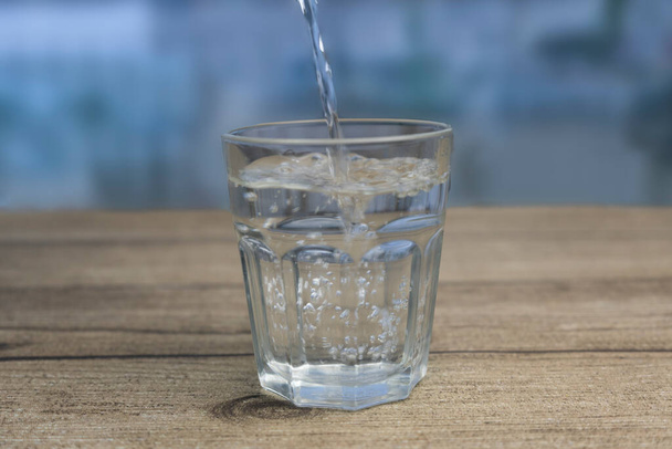 Fresh water pouring into glass on wooden table.Blurred background - Photo, Image