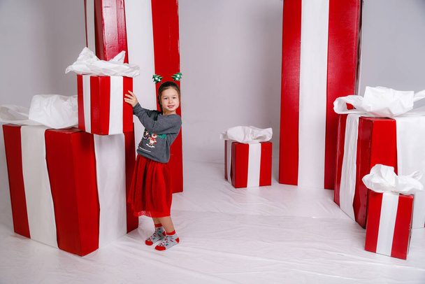 happy funny child girl in Christmas costume with big red gifts on background. - Fotoğraf, Görsel