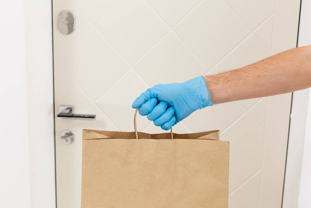 Courier in protective mask and medical gloves delivers takeaway food. Delivery service under quarantine, disease outbreak, coronavirus covid-19 pandemic conditions. - Foto, Bild