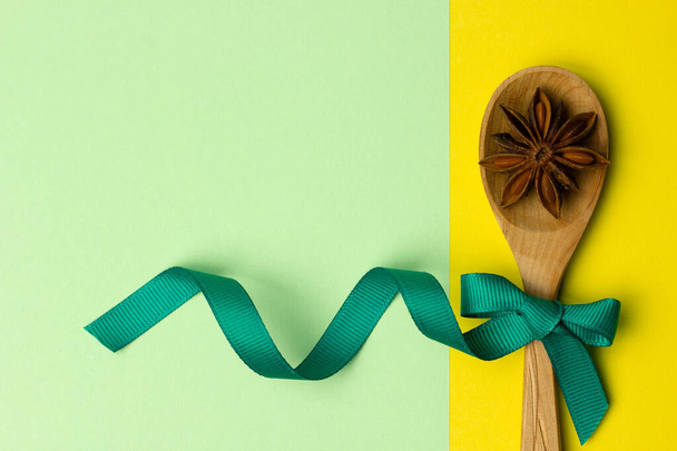 Trendiges Layout aus Kochlöffel und Anis mit Schleife auf grünem und gelbem Hintergrund. Aromatisierte asiatische Gewürze. Ferienkonzept. Flache Papierkarte. - Foto, Bild