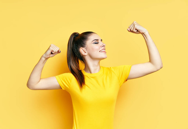 Powerful confident young woman showing arms muscles on yellow background - Φωτογραφία, εικόνα